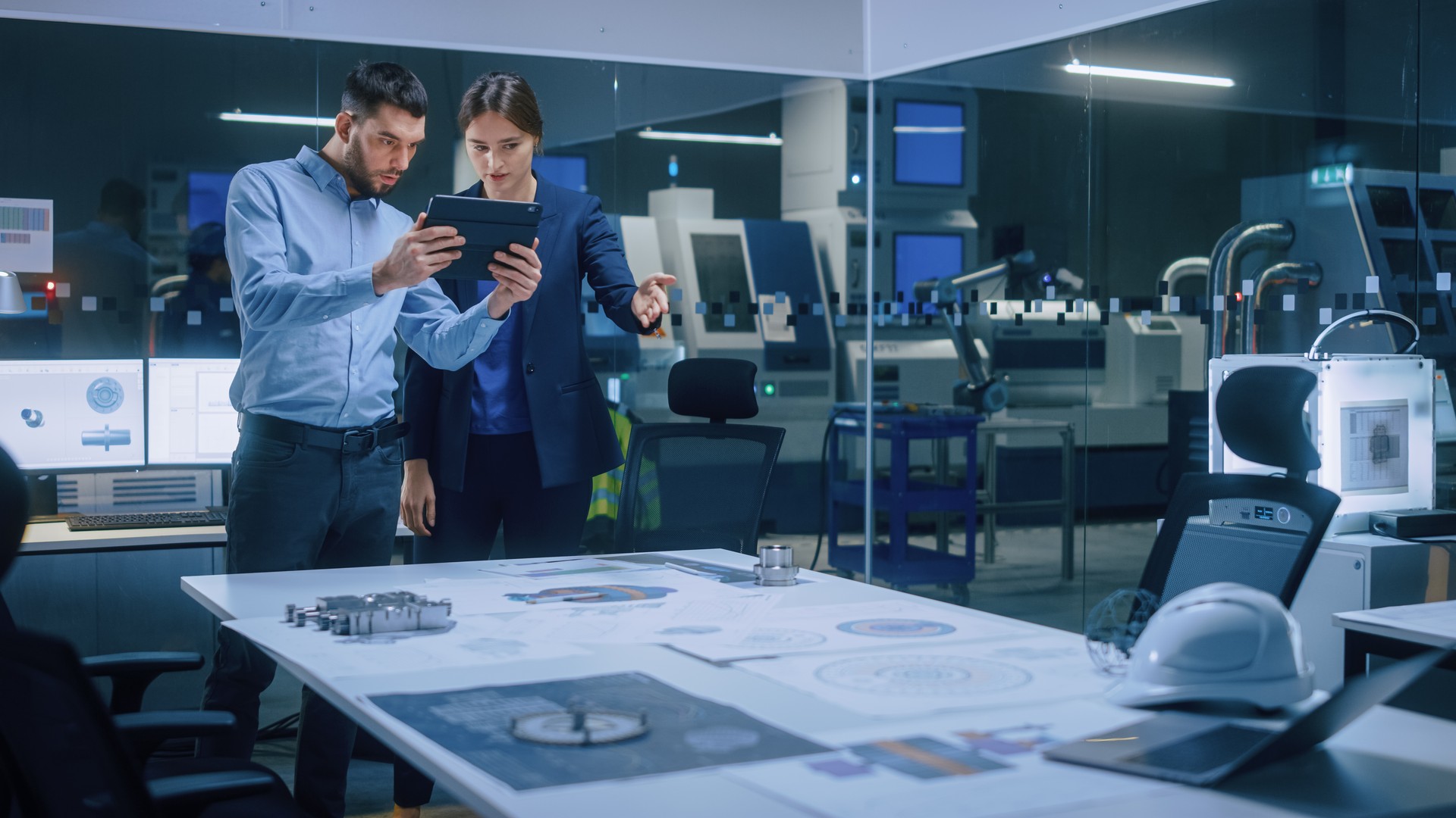 Factory Office Meeting Room: Male Chief Engineer Holds Digital Tablet Computer, Shows Screen to Female Project Manager, They Talk, Find Optimization Solution. Modern Industry 4.0 CNC Machinery